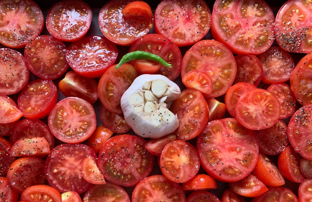 Photo: home-grown tomatoes, halved and ready to be roasted in the oven, a bulb of garlic with one clove missing, and a very hot chilli pepper.