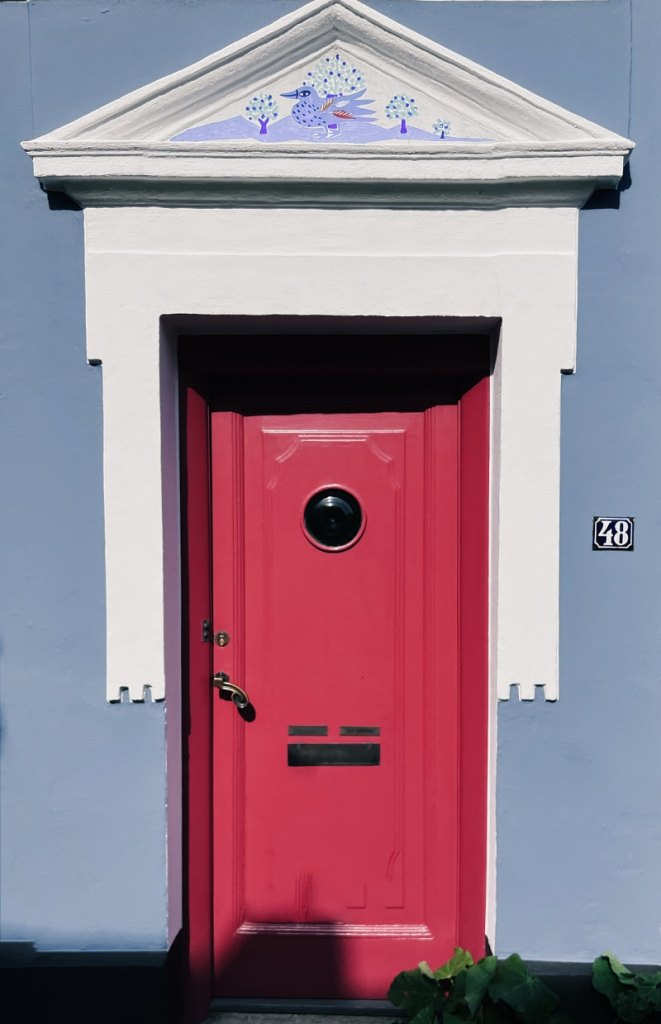 Red door, white frame, painting of a blue bird above the door.