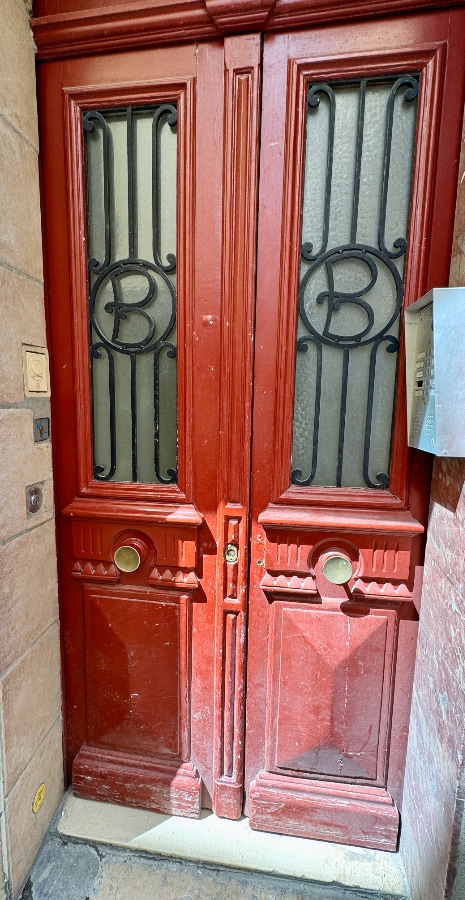 A double door painted red with wrought iron letter B inset in the windows