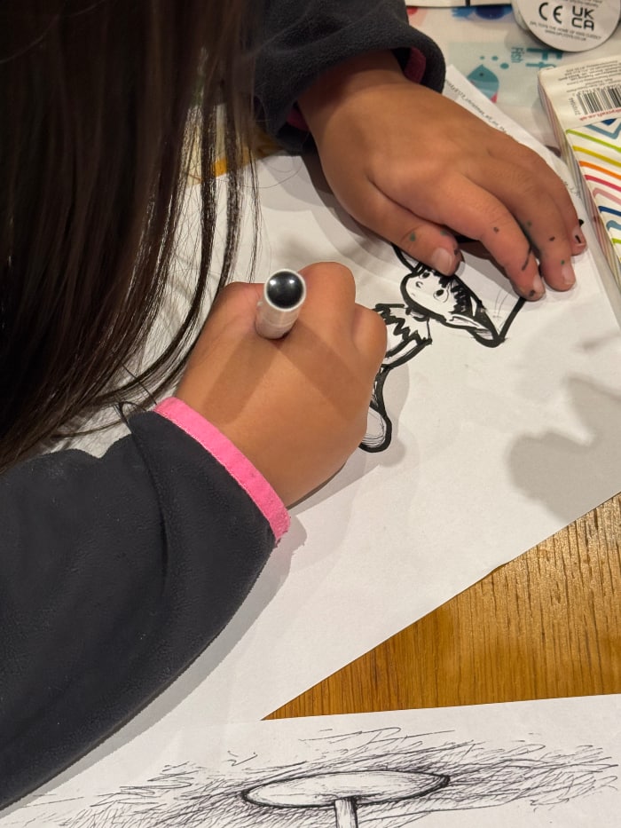 the hands of a child drawing a figure on a white sheet of paper with a black pen