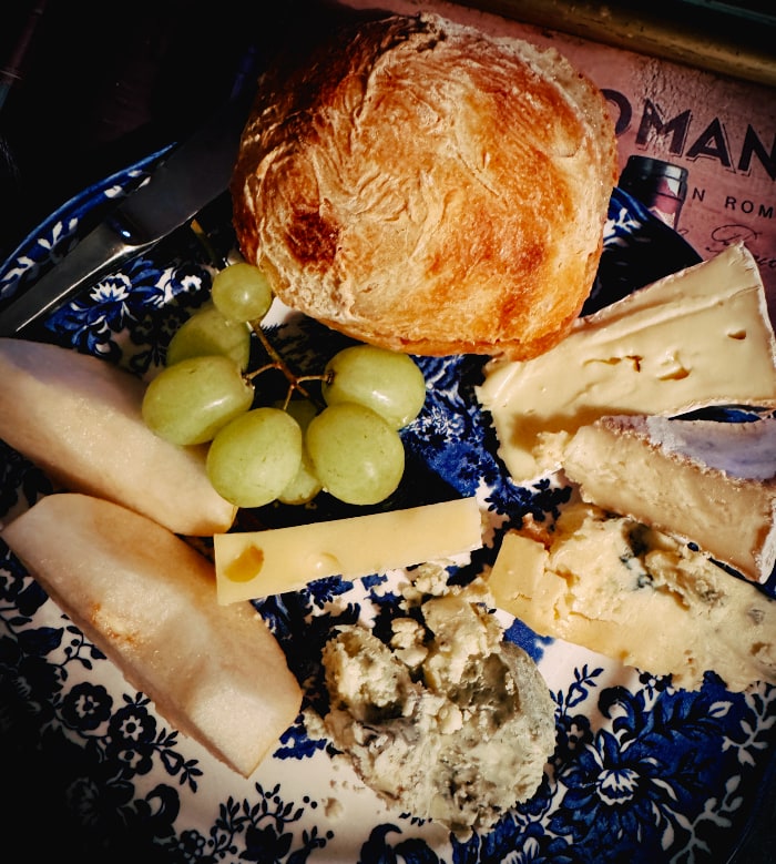 plate of various cheeses, grapes, pear and a big  crusty roll