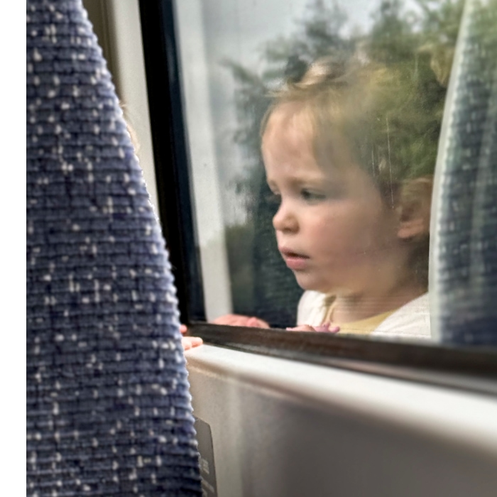 the reflection of a small girl looking out the window of a train