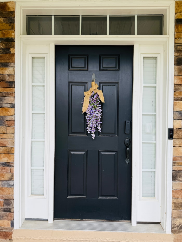 Black door with white surround with bouquet of wisteria
