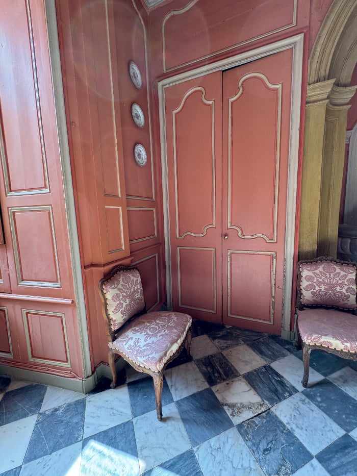 photo taken in French chateau of a bedroom, rose colour with white mouldings, and a door leading into another bedroom.