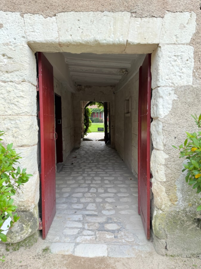 photo taken at Château de Chenonceau, Loire Valley, France, of double barn doors, red, open showing long hallway through the barn into a green garden area.