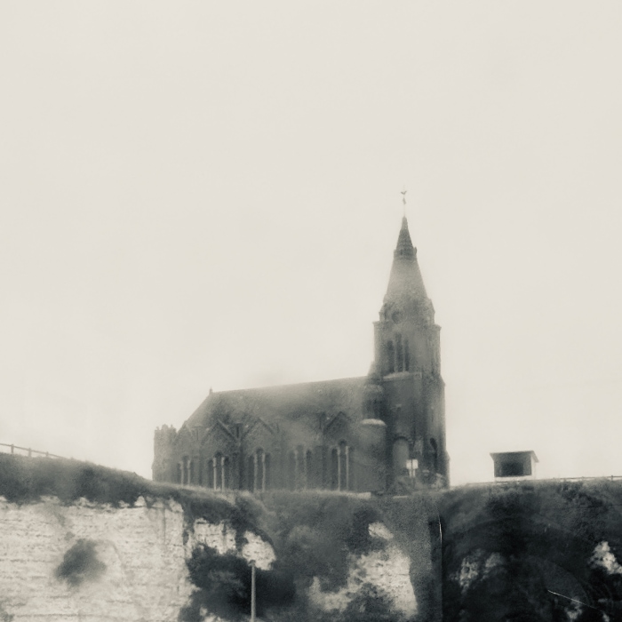 church with tall spire on the top of cliff overlooking Dieppe France and the sea on a rainy day with low clouds.