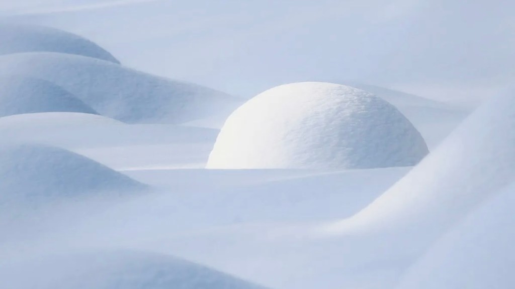 a snow-covered landscape with unique, rounded shapes. The colours reflected are white, light blue, and grey.