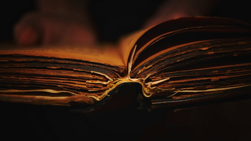 antique book open, warm colours of red and brown on a black background