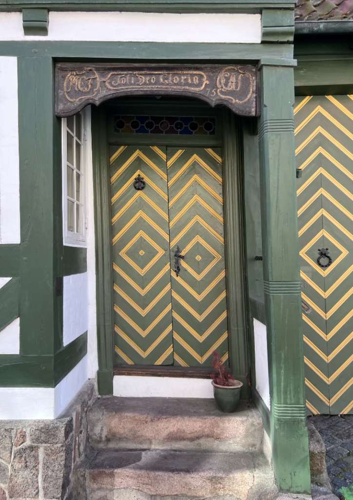 An ornate painted wooden door in Denmark, dated 1775, with geometric panels and the Latin inscription “Soli Deo Gloria” carved above it.